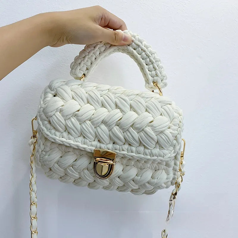 White braided handbag with gold accents held by a hand against a white background